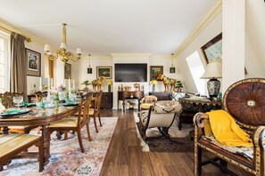 A spacious living room with a large wooden dining table, comfortable seating, and a flat-screen TV mounted on the wall.
