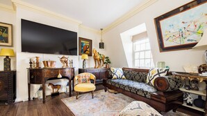 A spacious living room with a large flat-screen TV, a sofa, a chair, and a coffee table. - Mayfair 3-bed 6-guest W/patio & ac Berkeley Square (London)