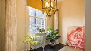 A hallway with a large window, a chandelier, a table with a vase of flowers, and a painting on the wall. - Mayfair 3-bed 6-guest W/patio & ac Berkeley Square (London)