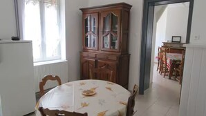 A dining area with a round table covered in a tablecloth, wooden chairs, a cabinet with glass doors, and a view into another room through an open doorway. - Maison Jardin Clos & Animaux Bienvenus - Near Lake & GR12 🐾 (Bourg-Fidèle)