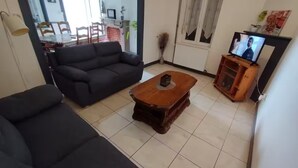 A living room with a dark sofa, a wooden coffee table, and a television on a wooden stand. - Maison Jardin Clos & Animaux Bienvenus - Near Lake & GR12 🐾 (Bourg-Fidèle)