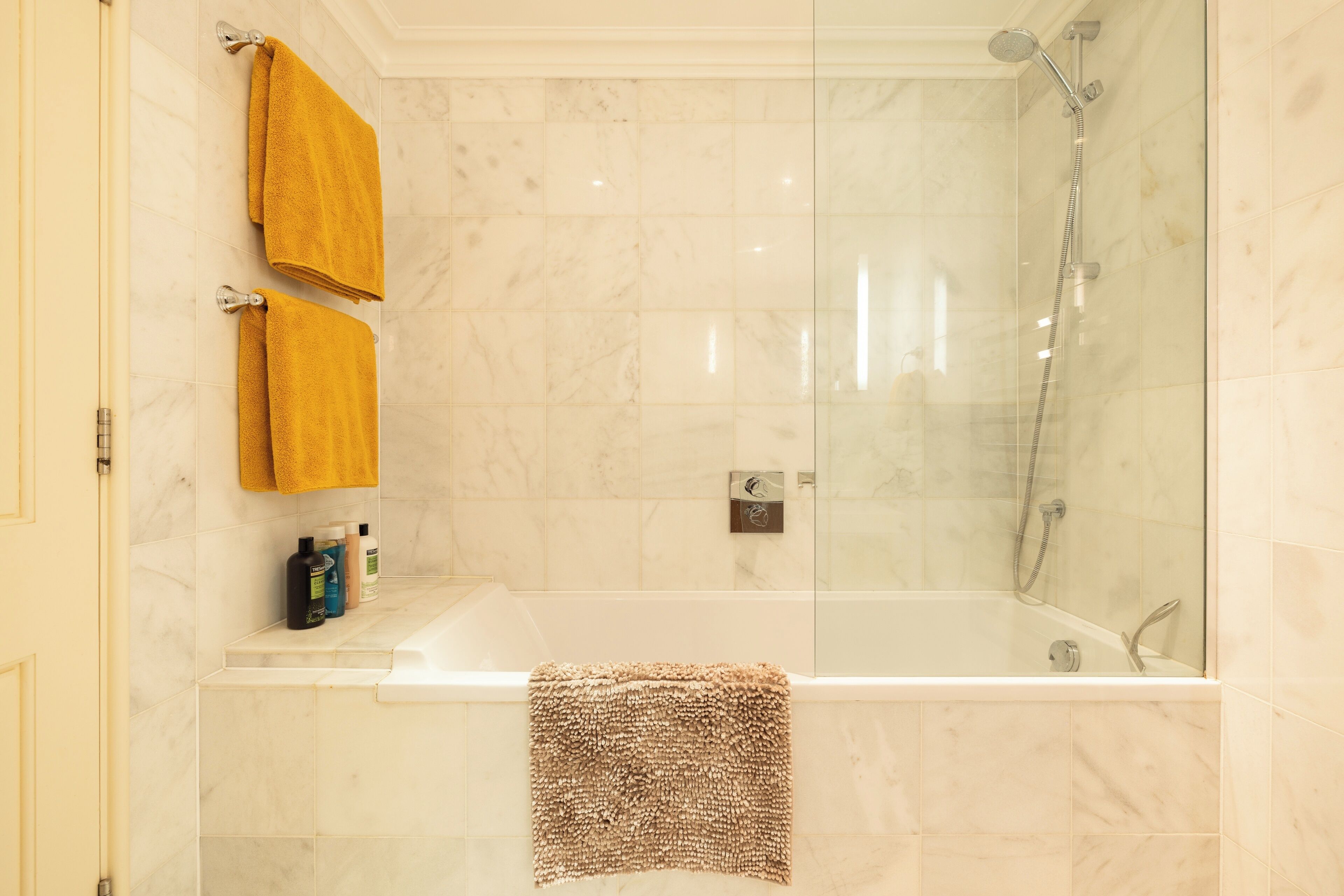 A modern bathroom with a glass-enclosed shower, a bathtub, and two towels hanging on the wall.