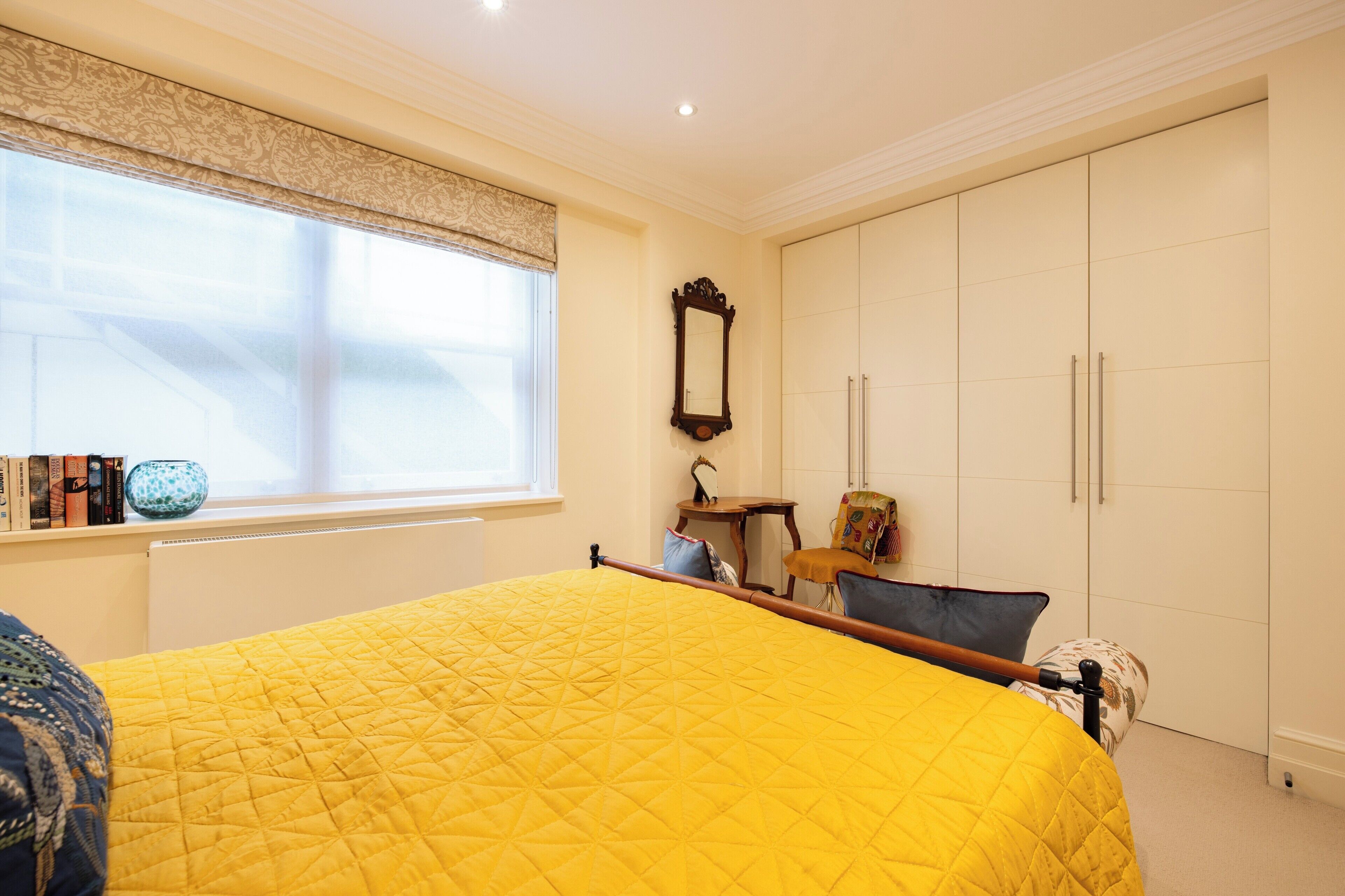 A bedroom with a large bed, a wardrobe, a window with a curtain, and a small table with a chair.