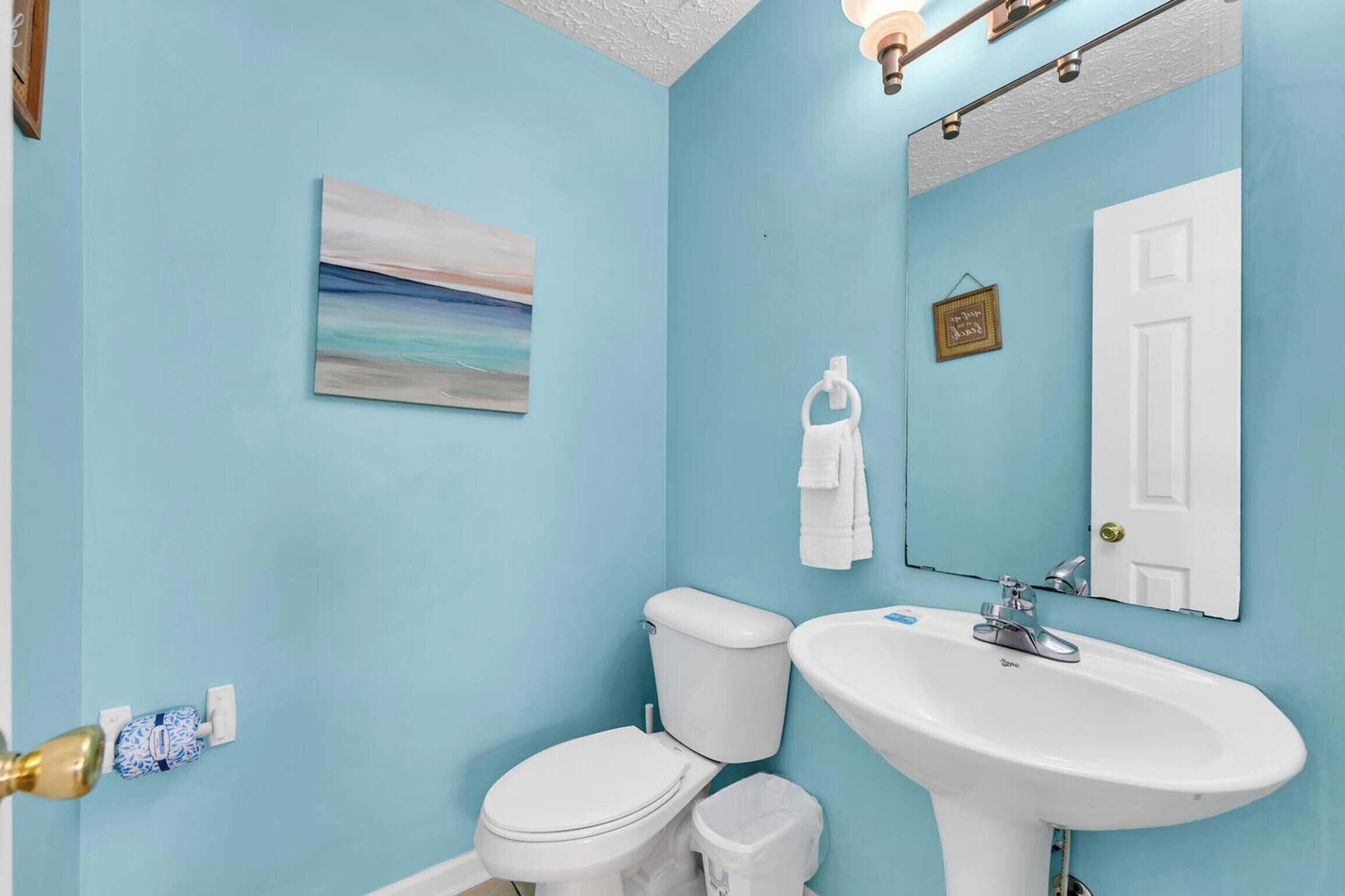 Un baño con pared azul, inodoro blanco, lavabo y espejo.