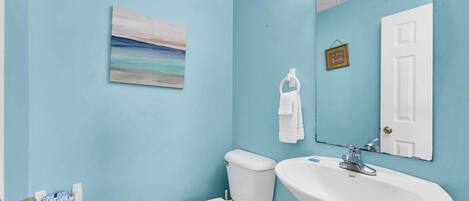 Un baño con pared azul, inodoro blanco, lavabo y espejo.