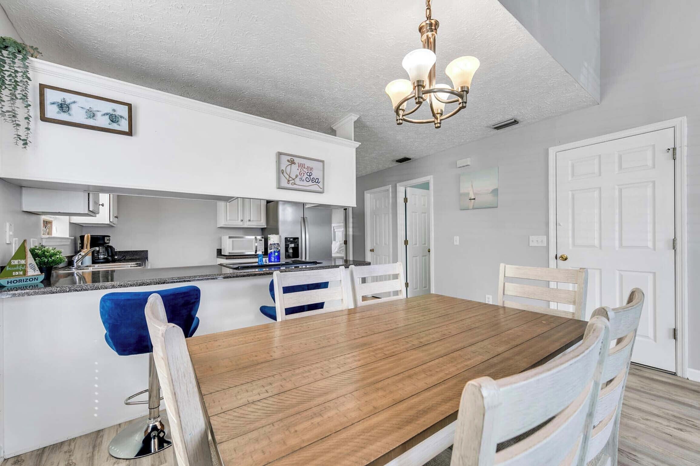 Una cocina moderna con armarios blancos, una mesa de comedor de madera y una araña.