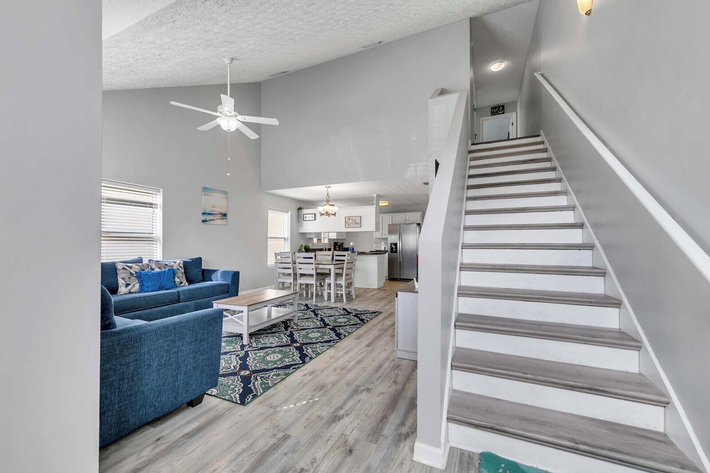 Un salon moderne avec un canapé bleu, un coin repas, une cuisine et un escalier.