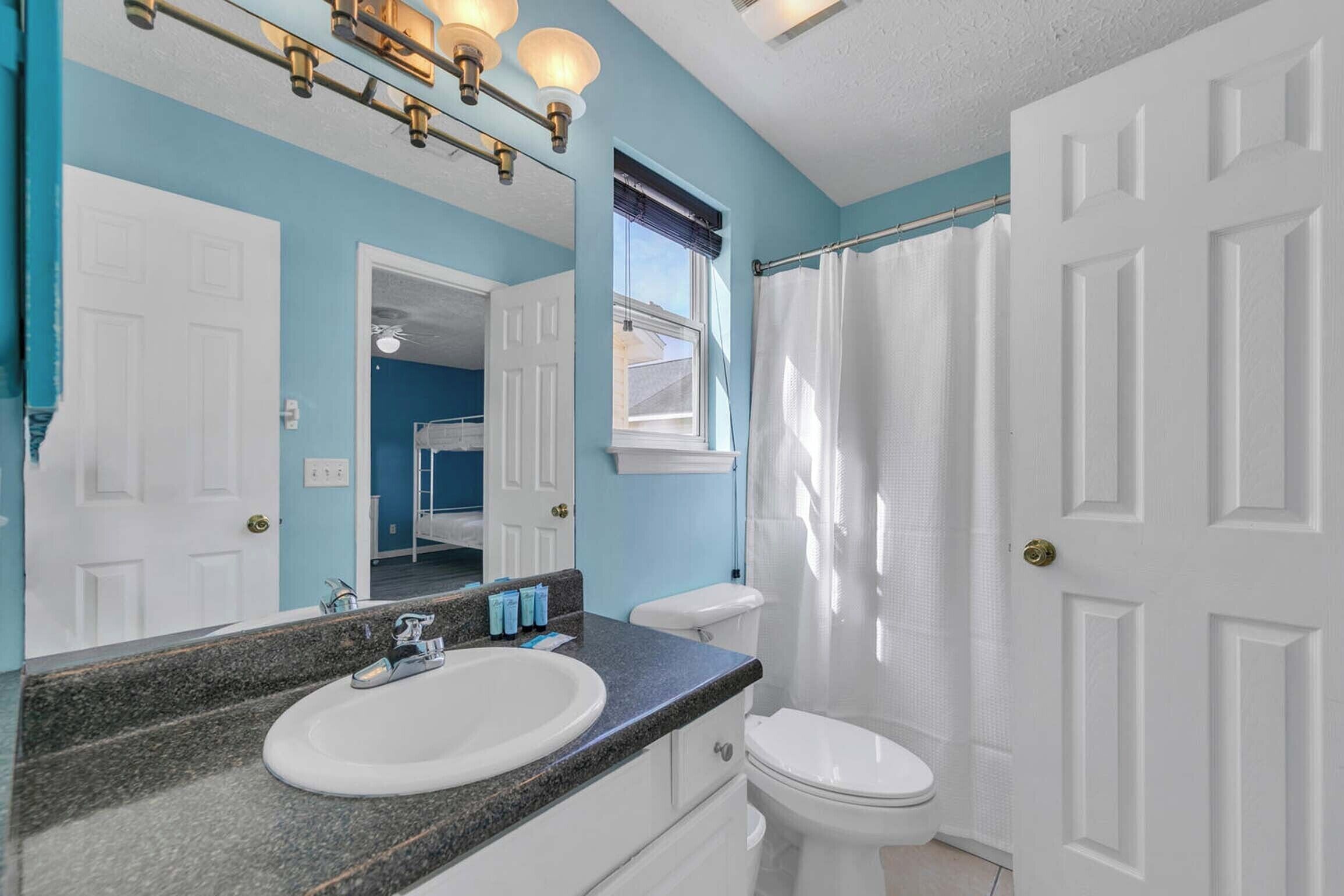 A bathroom with a white toilet, a sink with a granite countertop, and a shower curtain.