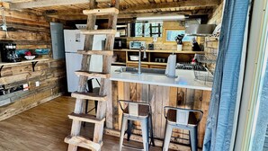 Une cuisine rustique avec des poutres en bois, un plan de travail blanc et des tabourets de bar en métal.