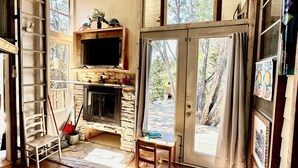 Un intérieur rustique avec une cheminée en pierre, des planchers en bois et de grandes fenêtres donnant sur l’extérieur.