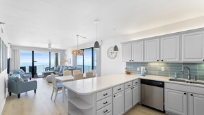 A modern kitchen with white cabinets, a central island, and a view to the outside. - 🌴🌊Romar Place 806: Beautiful Corner Unit | Beachfront (Orange Beach)