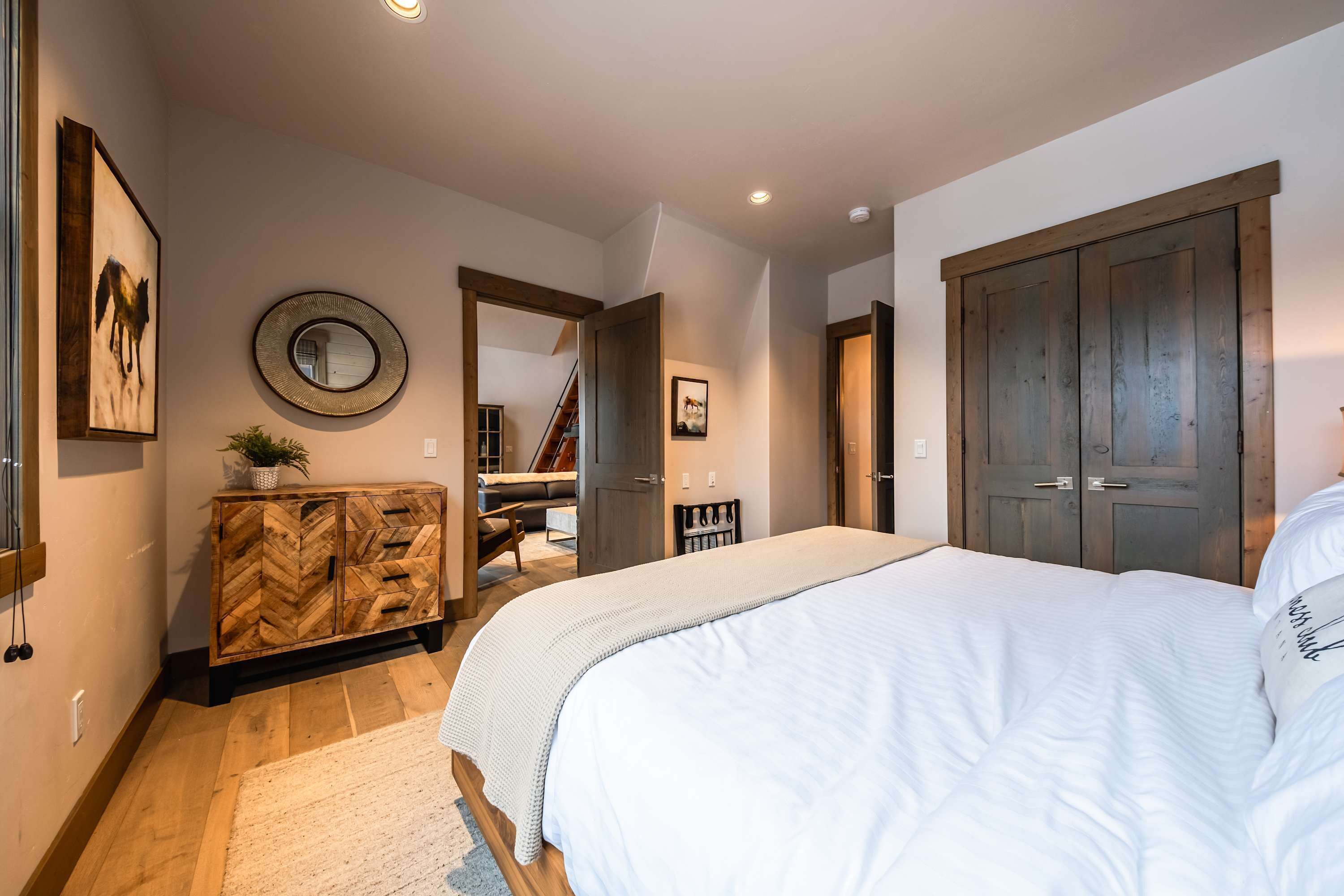 A bedroom with a large bed, wooden herringbone-patterned dresser, a round mirror, and a wooden wardrobe.