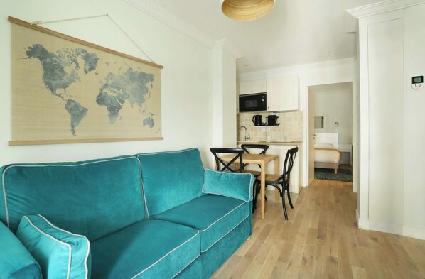 A teal sofa in a modern living room with a world map on the wall, a kitchen area with a microwave, and a dining table with chairs. - Apartment Center of Paris (Paris)