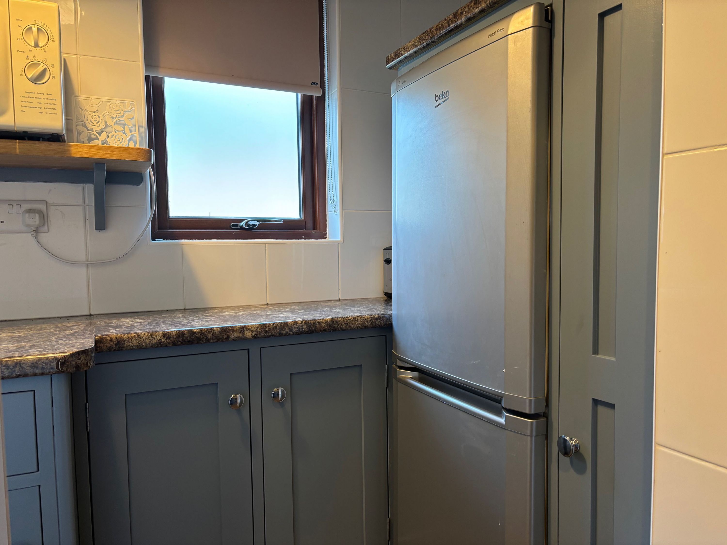 A kitchen with a built-in refrigerator, a window with a blind, and a countertop.