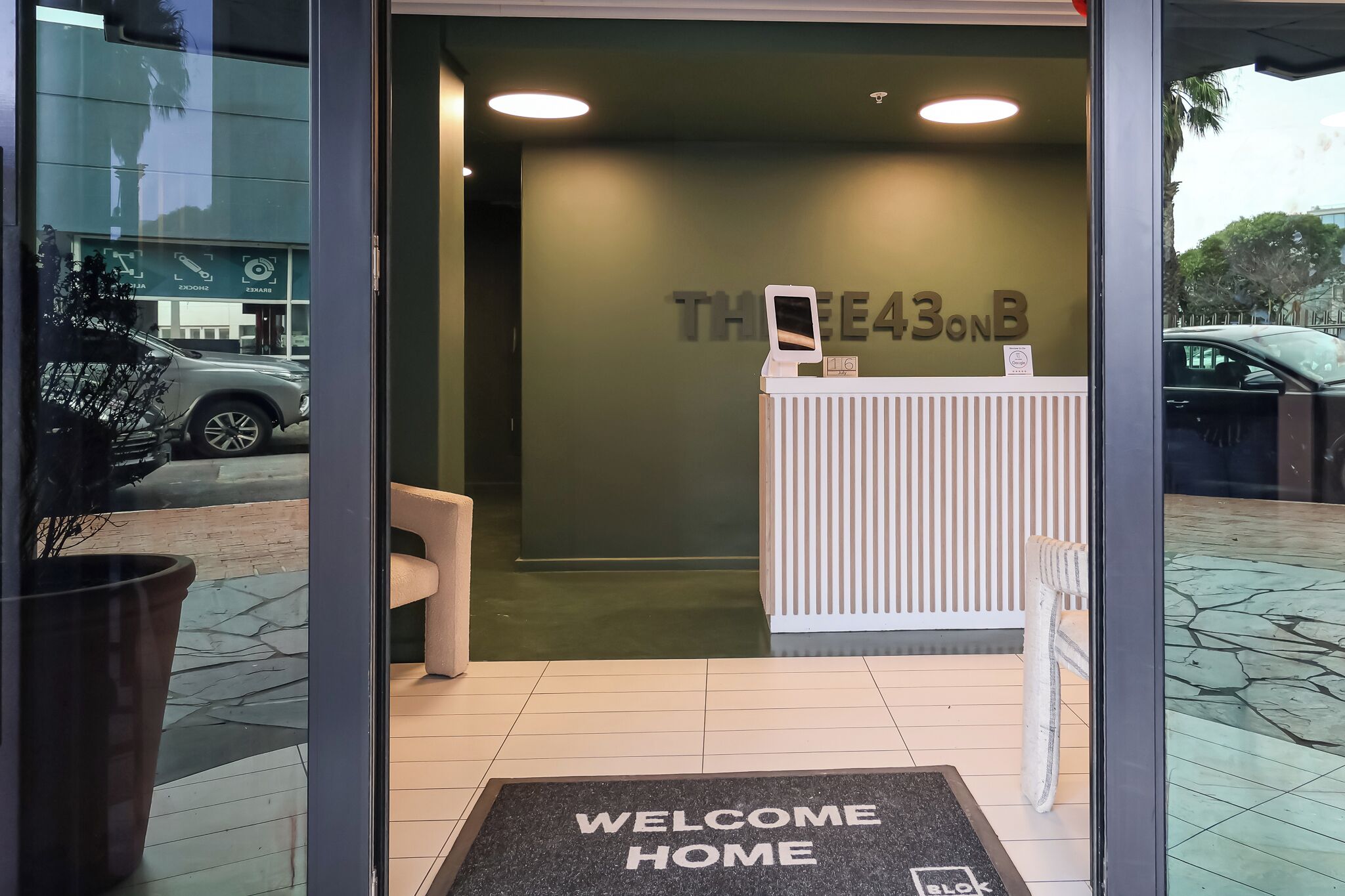 A reception area with a 'WELCOME HOME' mat, a reception desk, and a wall with the text 'THE 43ONB'.