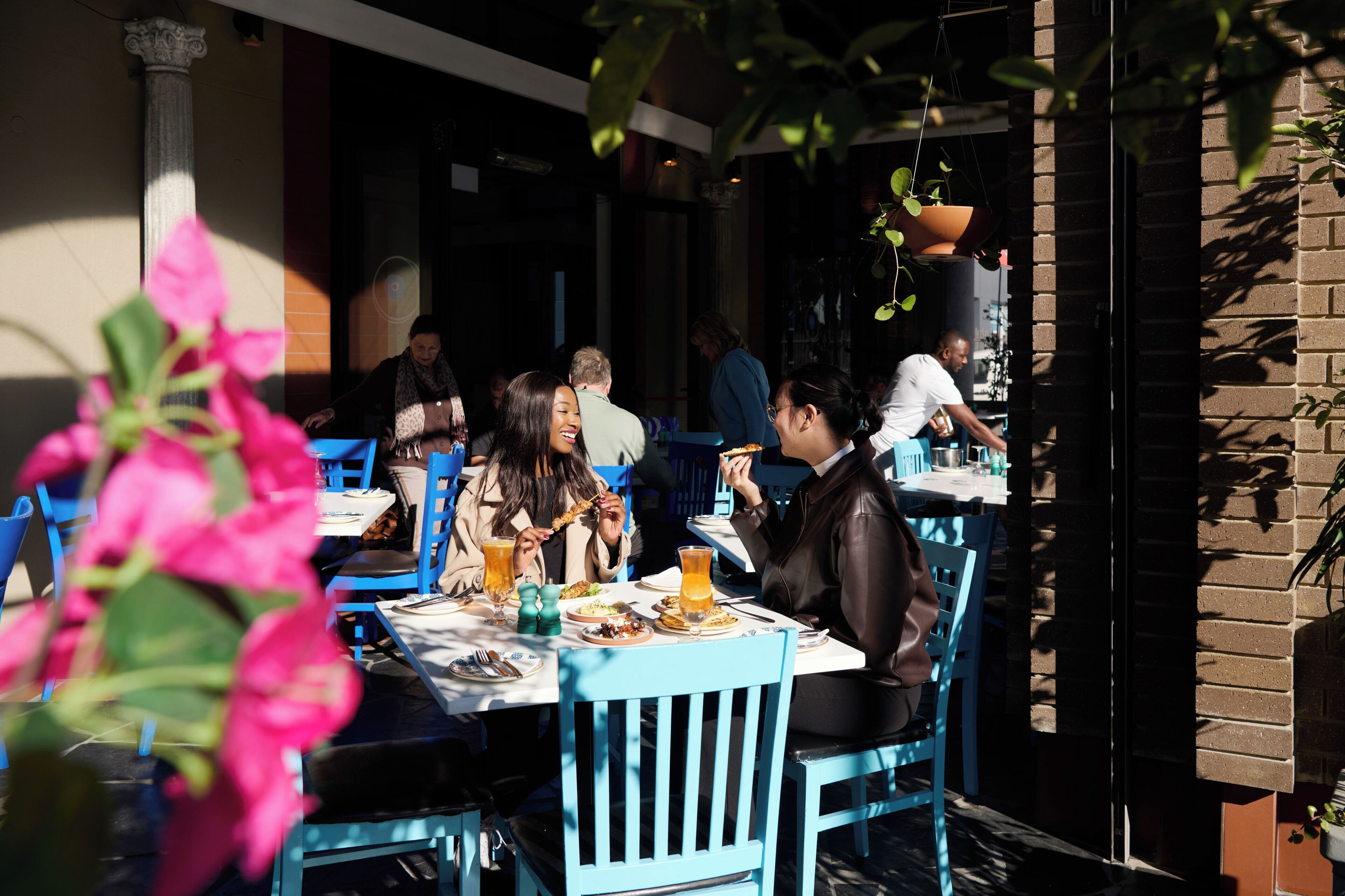 An outdoor dining area with tables and chairs, surrounded by brick walls and potted plants.
