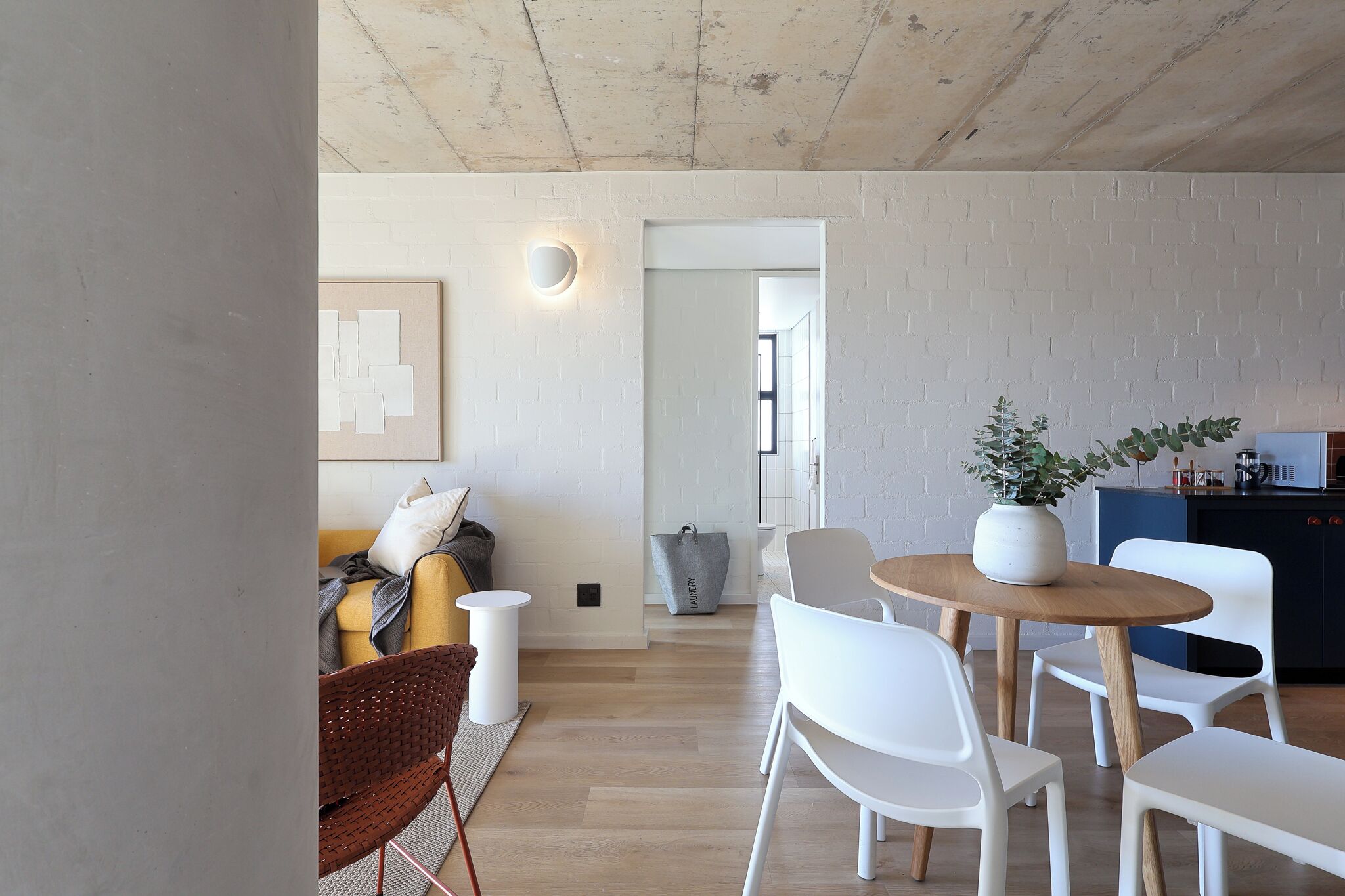 En moderne stue med sofa, stole, sofabord og et køkkenområde med en plante.