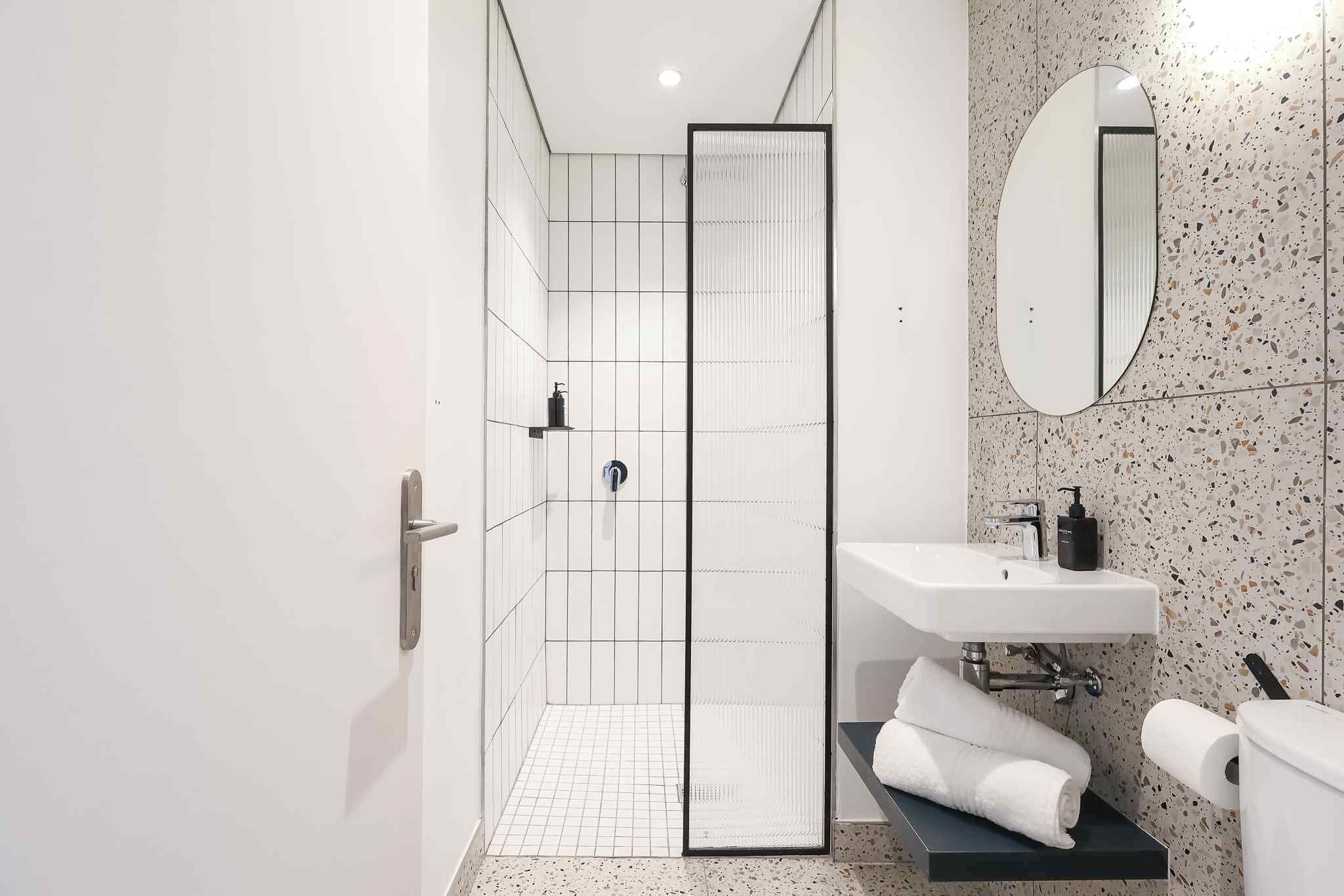 A modern bathroom with a shower, a sink, a mirror, and a towel rack.