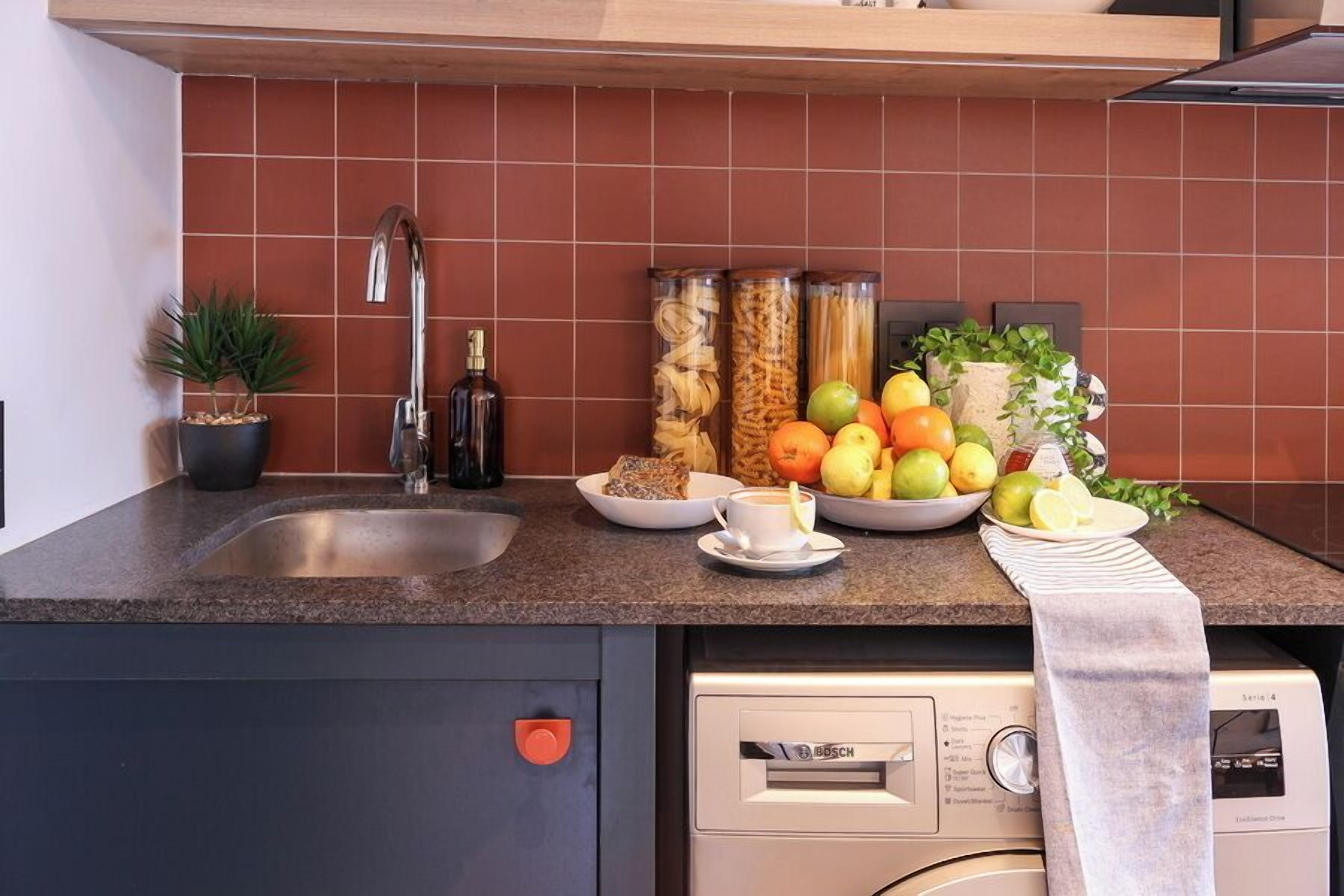 A kitchen with a sink, a Bosch dishwasher, and various food items on the counter.