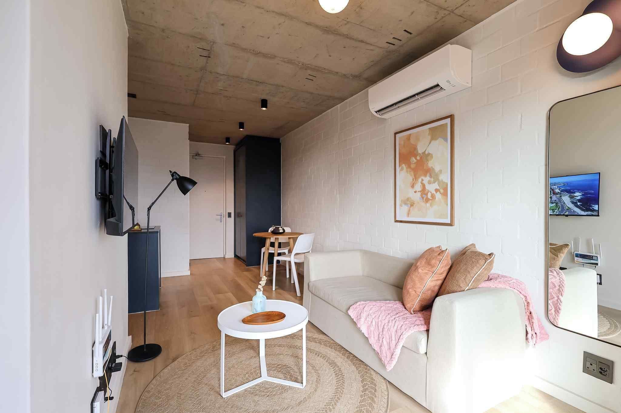 A modern living room with a white sofa, a round coffee table, a flat-screen TV, and a large mirror.