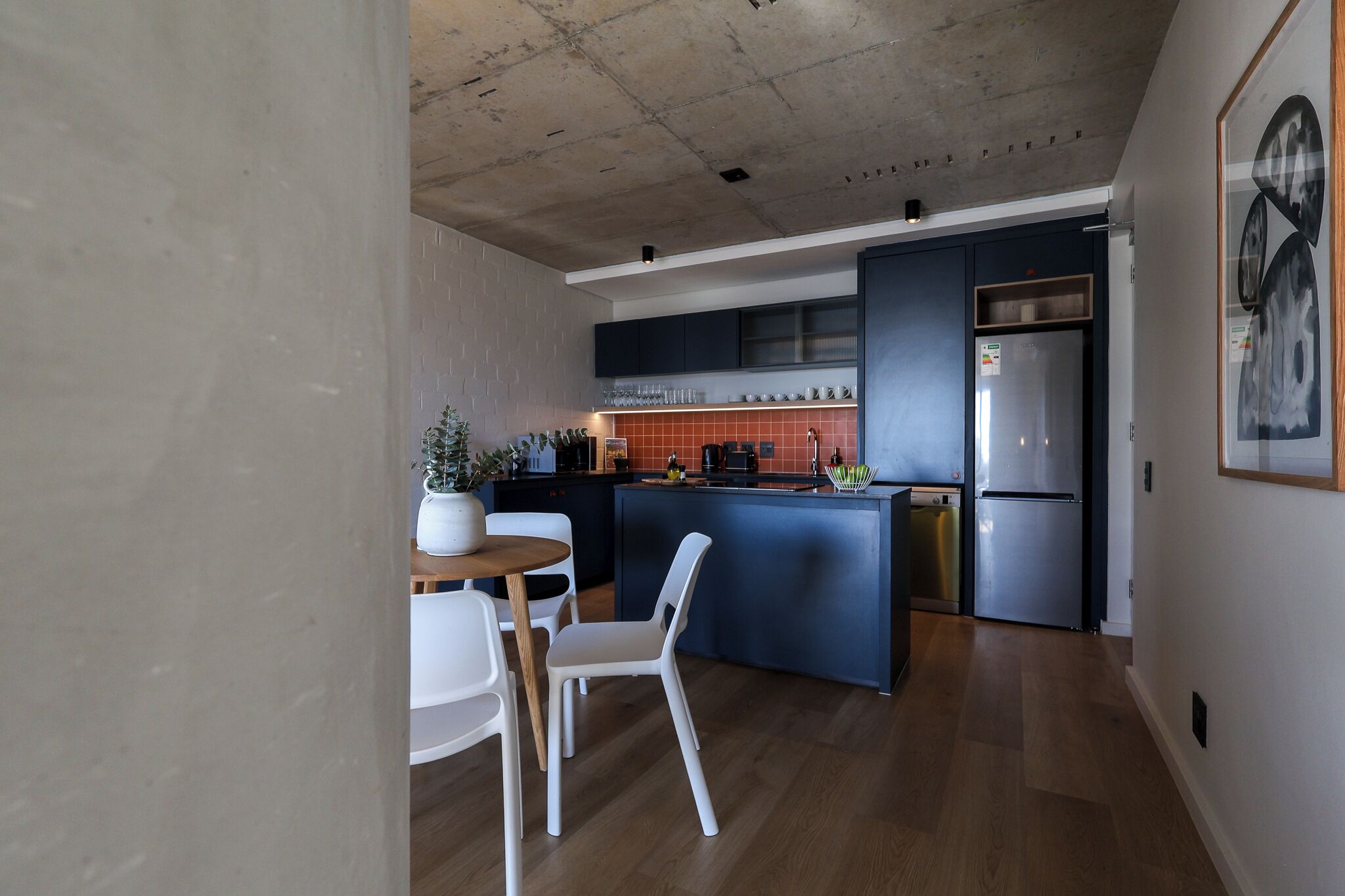 Una cocina moderna con una isla central, un comedor con una mesa redonda y sillas, y un refrigerador grande.