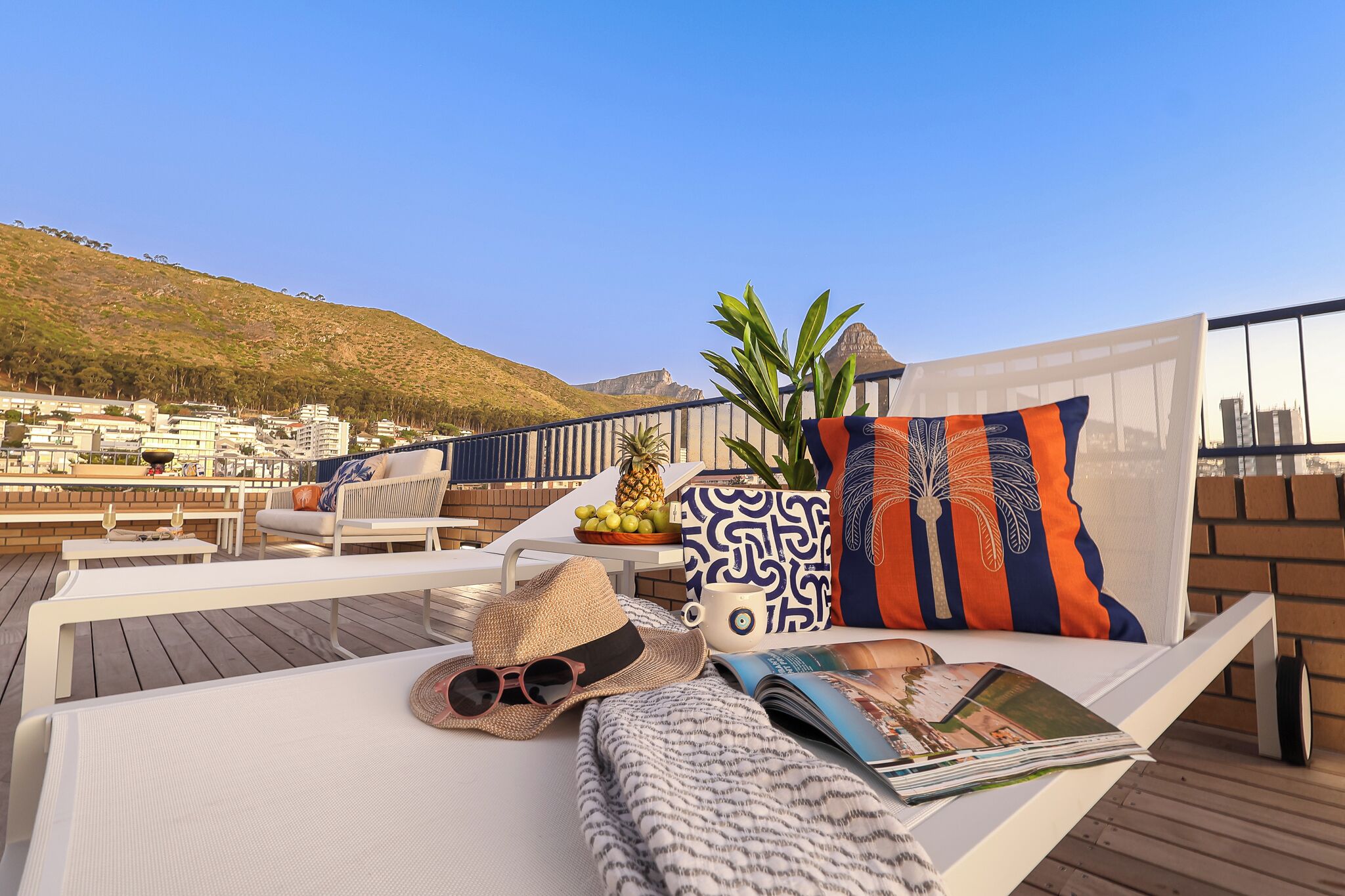 A sunlit outdoor seating area with lounge chairs, a table, and a view of a hillside.