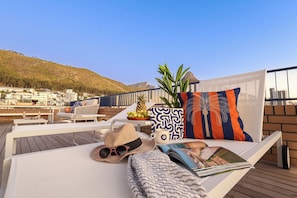 A sunlit outdoor seating area with lounge chairs, a table, and a view of a hillside. - THREE43 on B - Fluent Serviced Apartments (Cape Town)