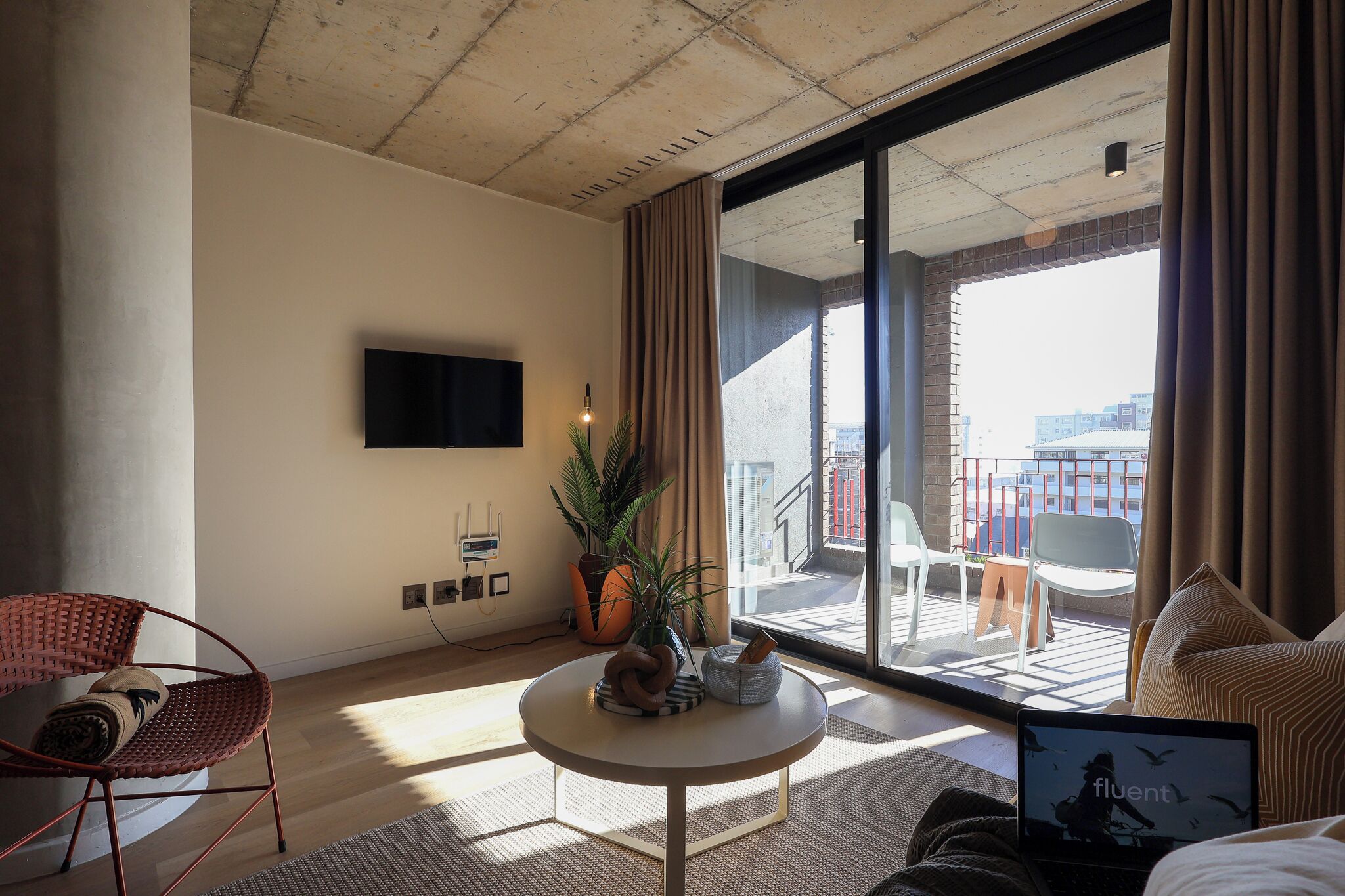 Habitación de hotel moderna con un balcón grande, televisor de pantalla plana, una mesa redonda con adornos y una zona de estar cómoda.