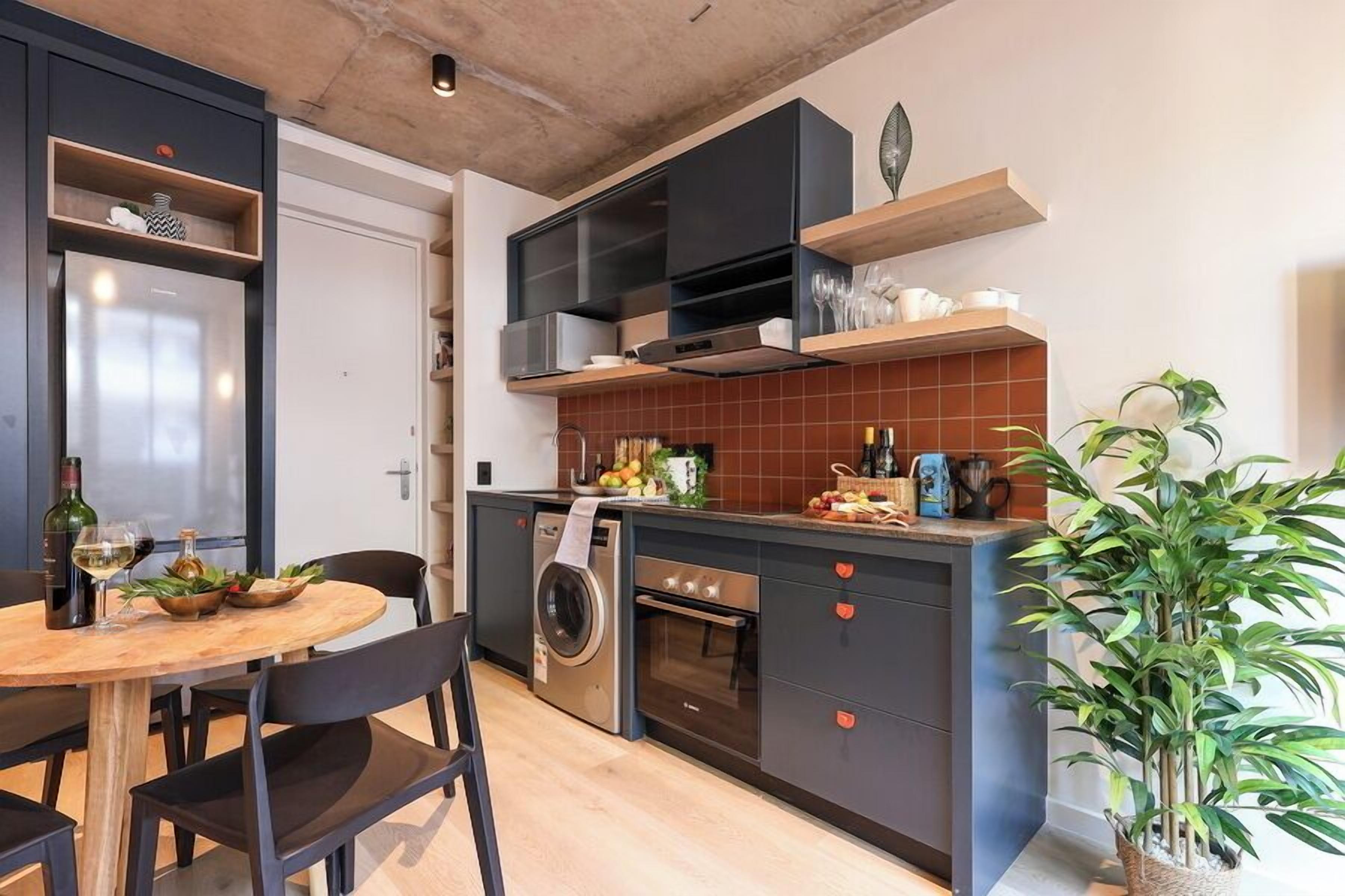 Een compacte keuken met een ingebouwde wasmachine, een klein oven en een eethoek met een ronde tafel en stoelen.