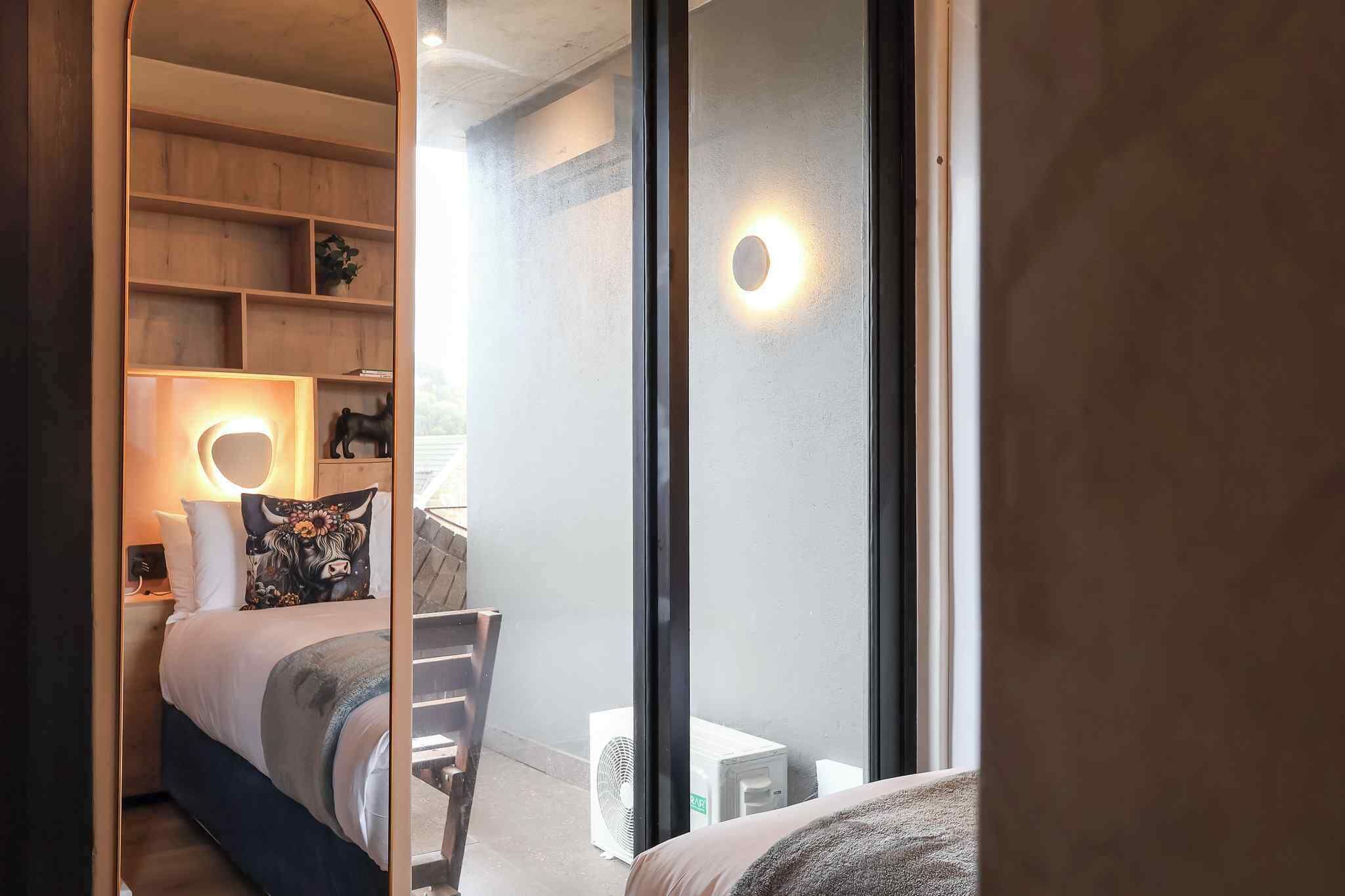 A bedroom with a bed, bedside table, lamp, and a view through a glass door.
