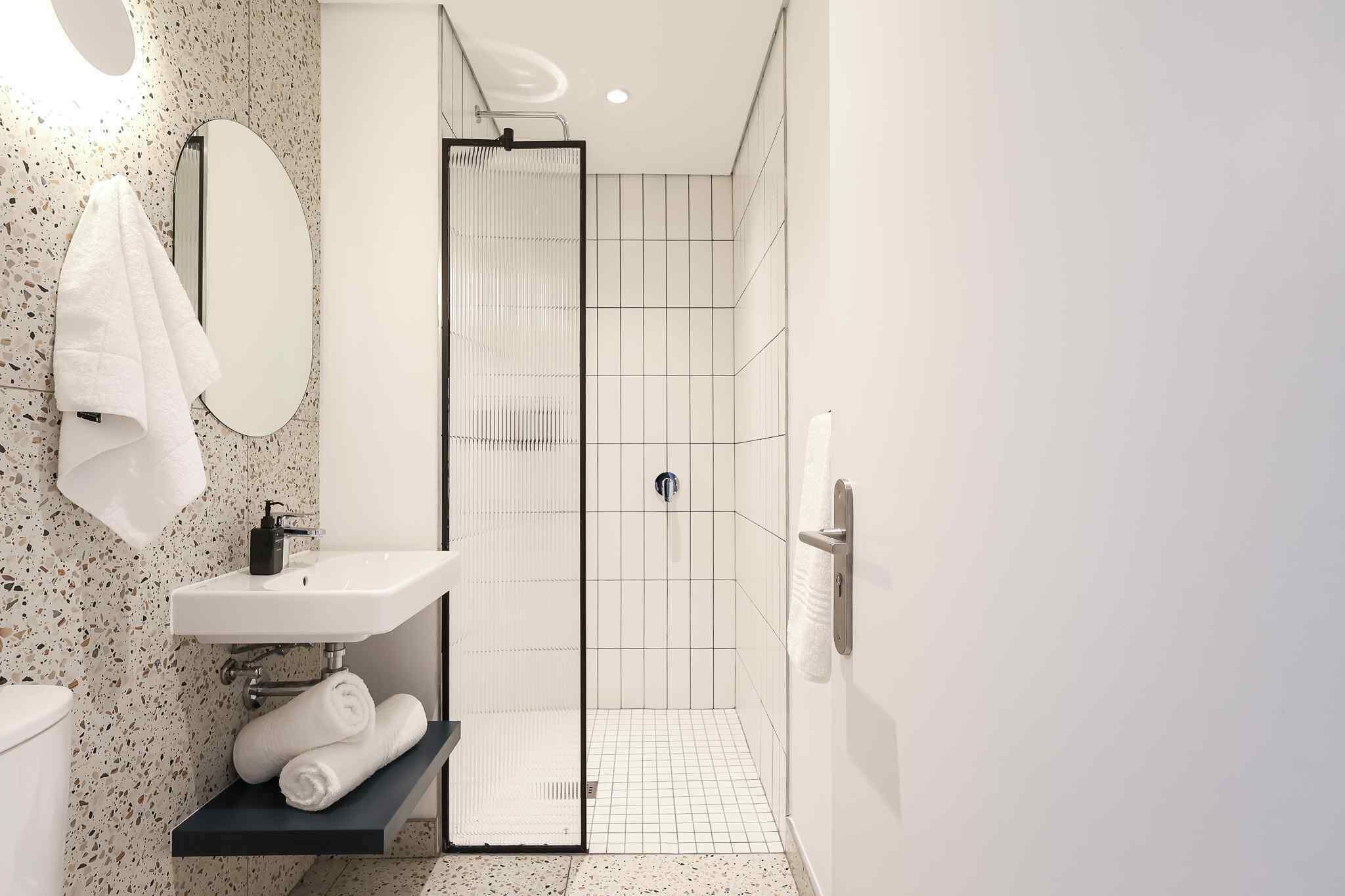 Een moderne badkamer met een douche, wastafel en handdoekrek.