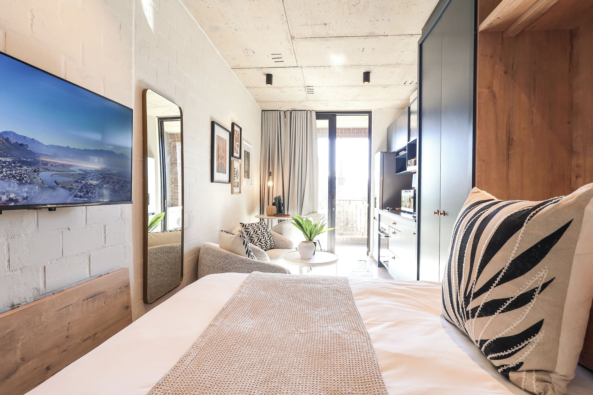 A modern bedroom with a large bed, a seating area with a table, and a view of a cityscape through a window.