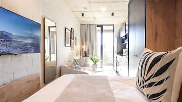 A modern bedroom with a large bed, a seating area with a table, and a view of a cityscape through a window.