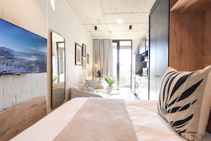 A modern bedroom with a large bed, a seating area with a table, and a view of a cityscape through a window. - THREE43 on B - Fluent Serviced Apartments (Cape Town)