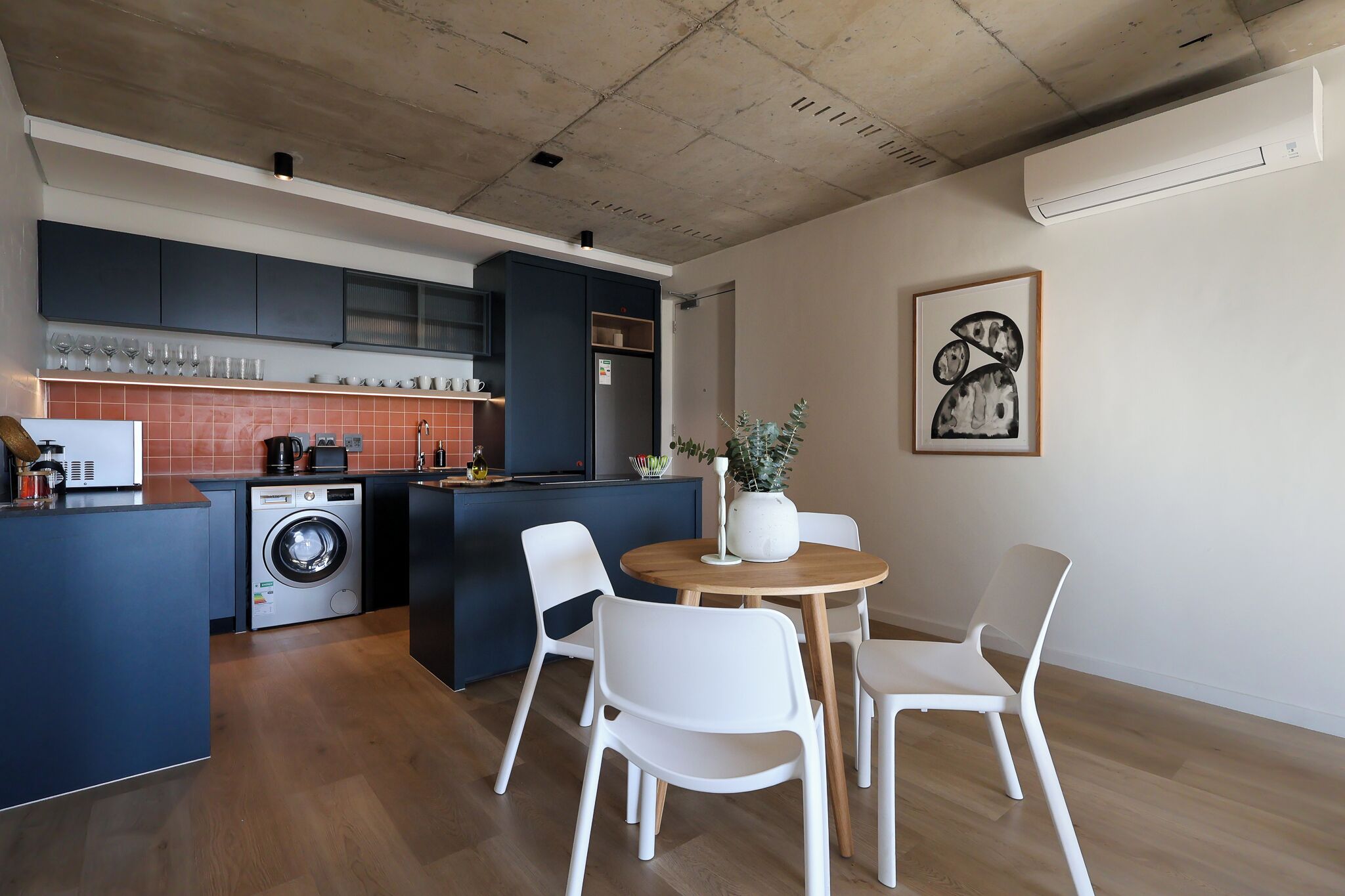 Una cucina funzionale con lavatrice, un'area pranzo con tavolo rotondo e sedie bianche, e un'ampia finestra.