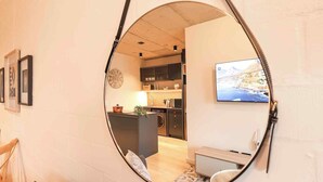 Une cuisine moderne équipée d’un téléviseur à écran plat, d’un coin repas avec une table et des chaises, et d’un grand miroir qui reflète la pièce.