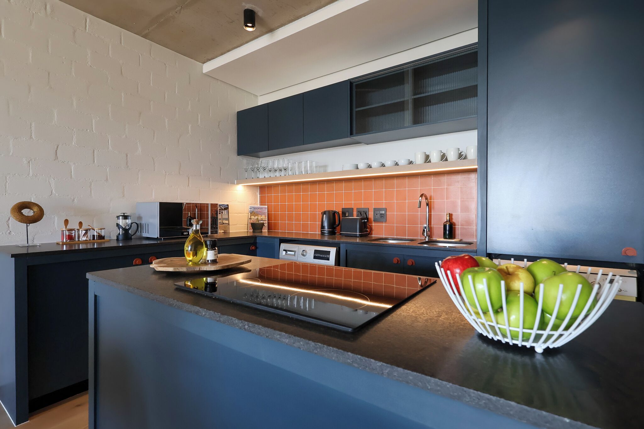 Una cucina moderna con isola centrale, elettrodomestici integrati e una parete rivestita.