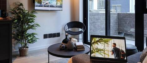 A modern living room with a flat-screen TV, a laptop, a potted plant, and a black chair.