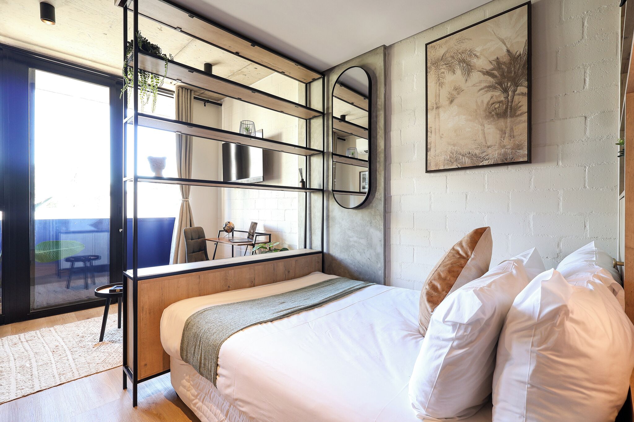 A modern bedroom with a bed, a large mirror, a painting, and a view of the outside.