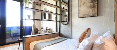 A modern bedroom with a bed, a large mirror, a painting, and a view of the outside.