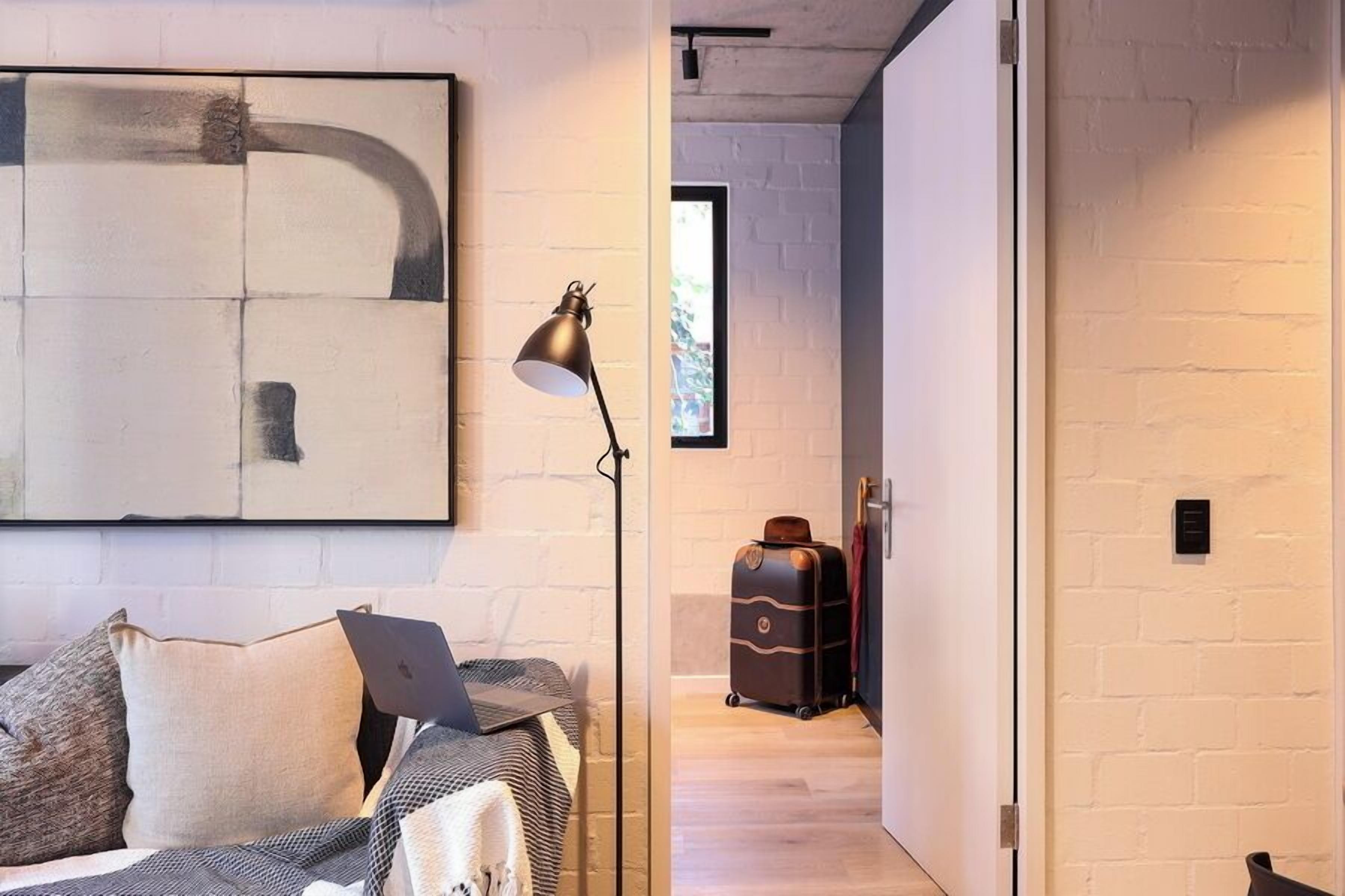 Una camera d'albergo moderna con un letto, un portatile, una lampada da terra e una valigia sullo sfondo.