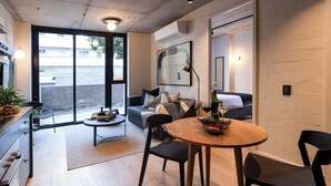 Un salon moderne comprenant un coin repas, un canapé, une table basse et une cuisine visible à travers une porte ouverte.