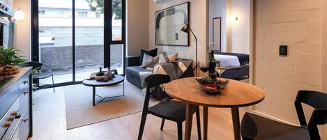 A modern living room with a dining area, a sofa, a coffee table, and a kitchen visible through an open door.