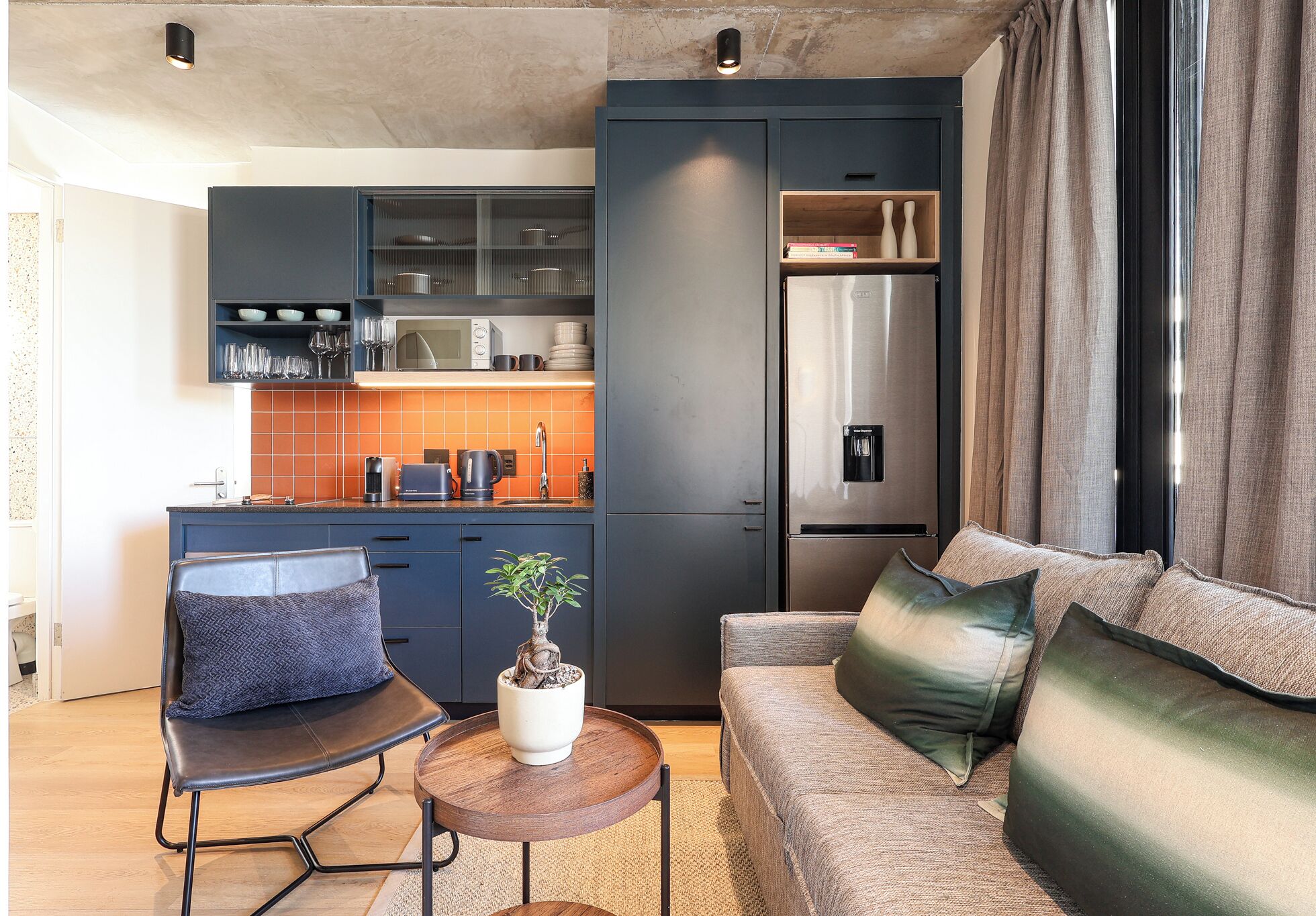 A compact living space with a kitchenette, a sofa, a chair, and a small table with a potted plant.