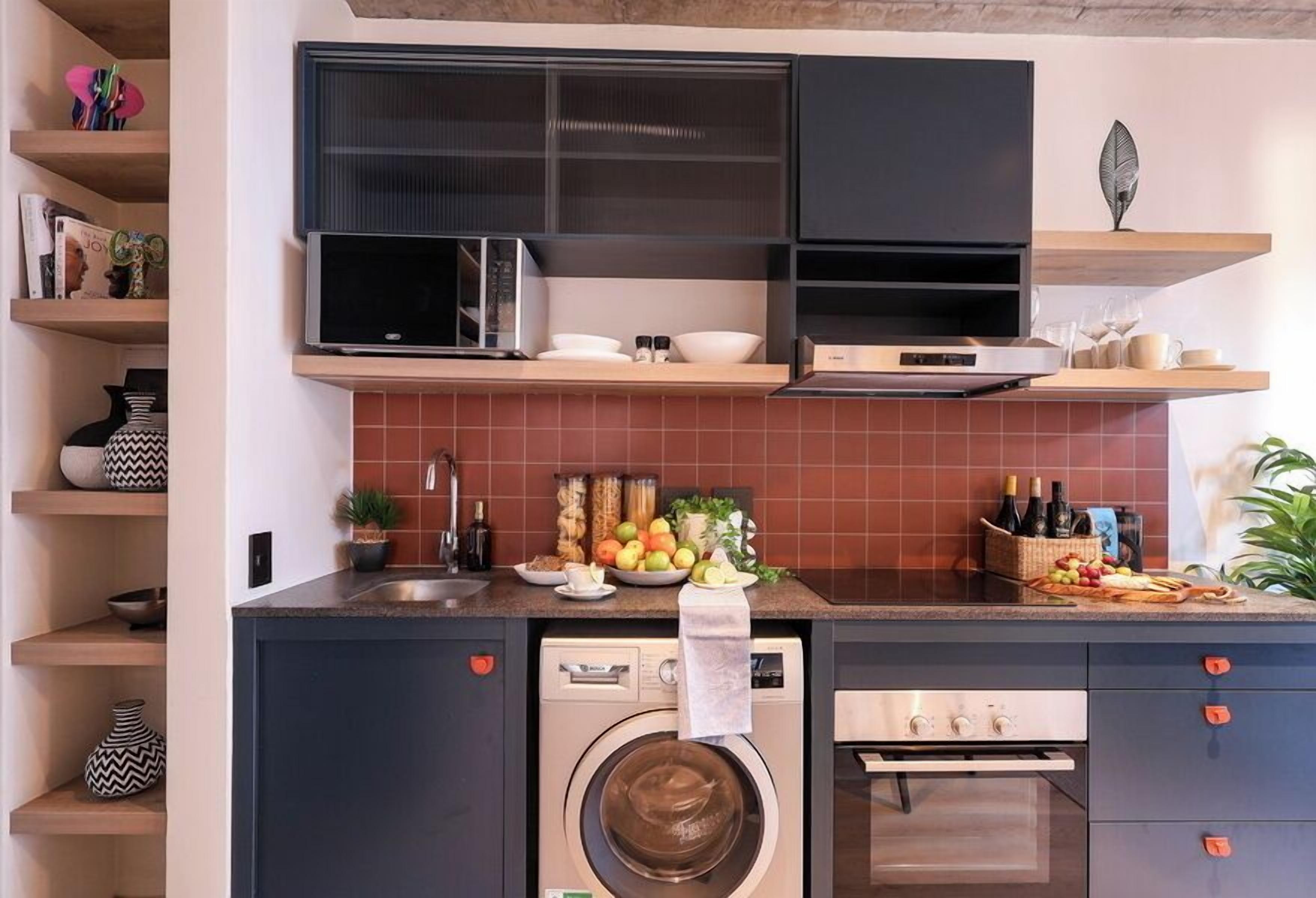 Una cucina compatta con lavatrice, forno, microonde ed scaffali con stoviglie.