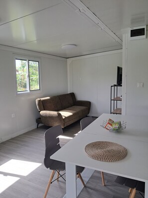 A room with a white table, a brown sofa, and a window with a view of greenery.