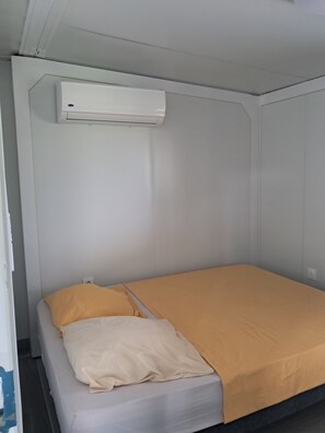 A single bed with a beige and yellow bedspread, a white pillow, and an air conditioning unit mounted on the wall above.