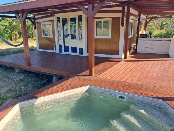 A wooden deck with a pool, a covered area with sliding glass doors, and a kitchen area.