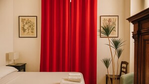 A hotel room with a bed, red curtains, a nightstand with a lamp, two framed botanical illustrations, and a potted plant. - Casa Milano Vintage Vibes with balcony (Milan)