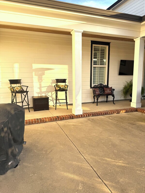 A covered patio area with two chairs, a bench, and a barbecue grill.